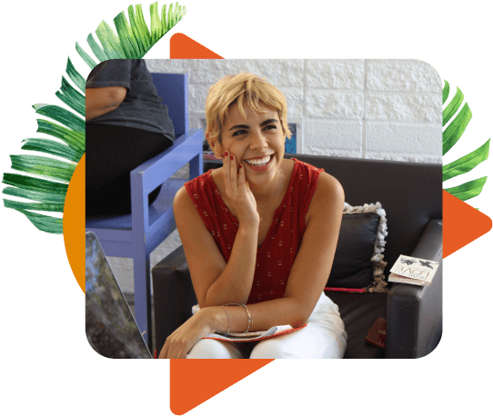 A young woman with short blonde hair smiling up at the camera while seated in a lounge chair indoors