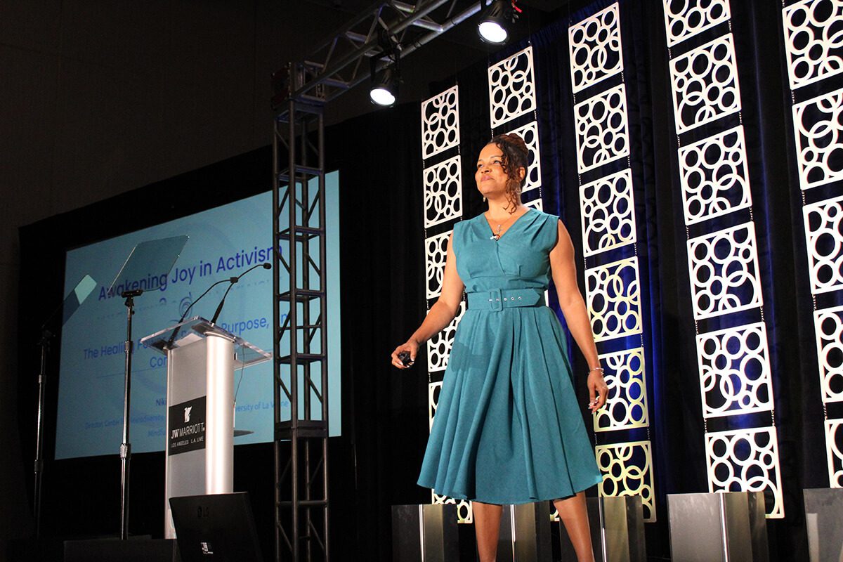 Dr. Niki speaking on a large stage in a teal blue dress