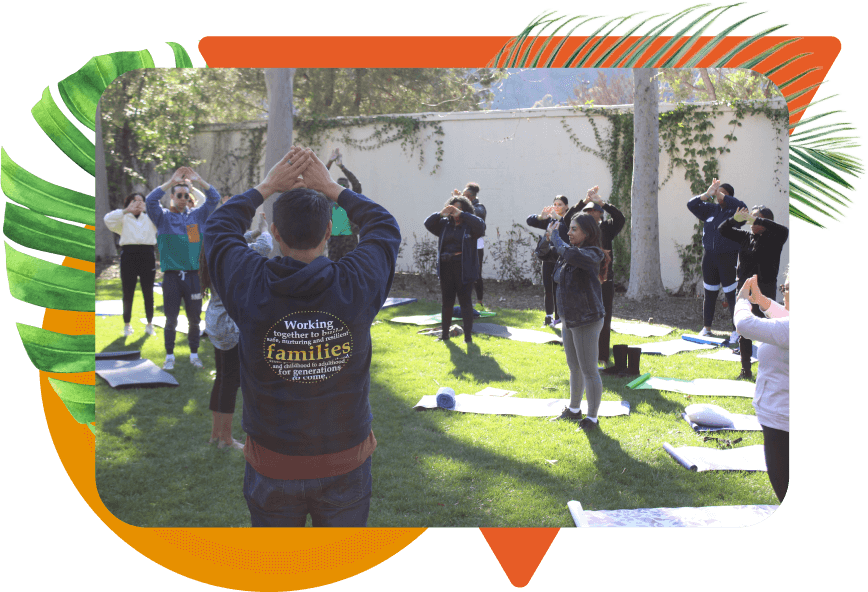 A diverse group of individuals with their arms together above their head while standing next to yoga mats outdoors